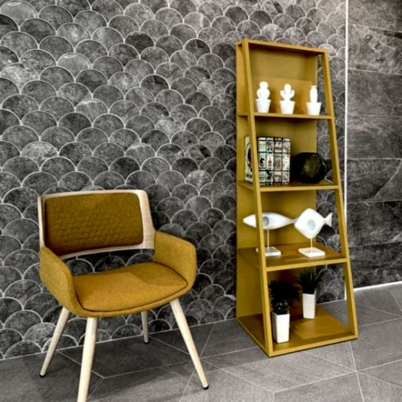 Scale Concrete Grey Scallop Shape Tiles on a wall. A lovely mustard chair and bookcase with ornaments are a focal point.